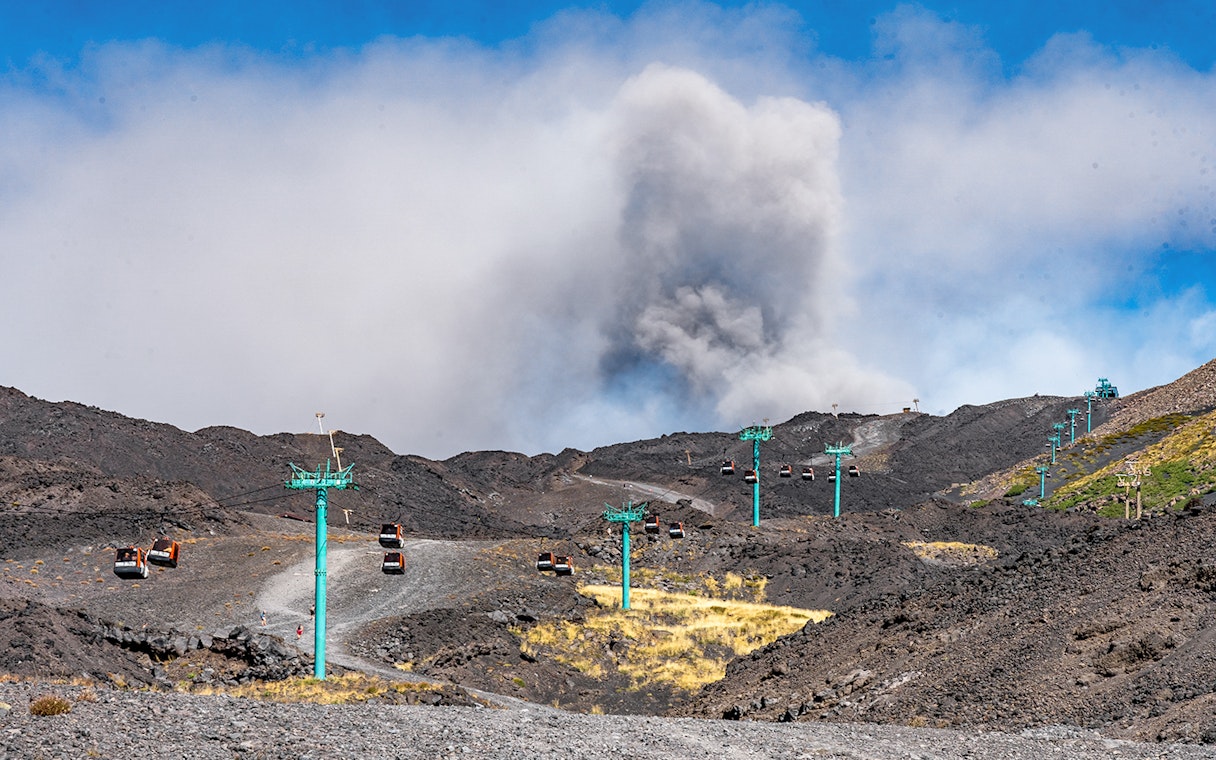 Cable car ascending Mount Etna with volcanic crater in background, Sicily.