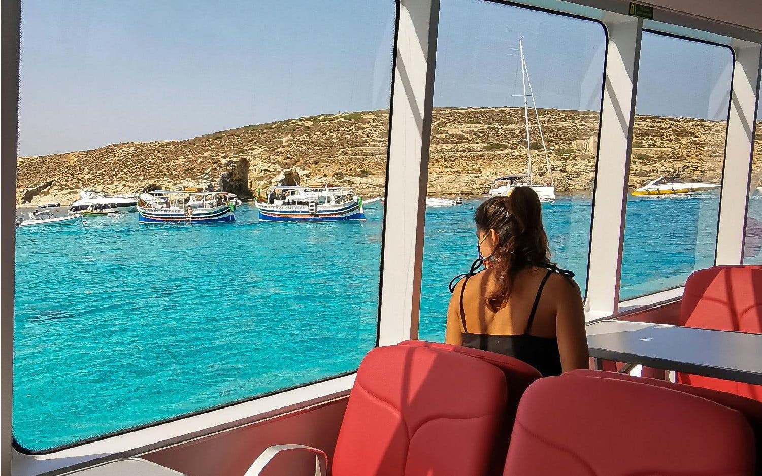 Tourist inside boat viewing Blue Lagoon's turquoise waters and rocky coastline.