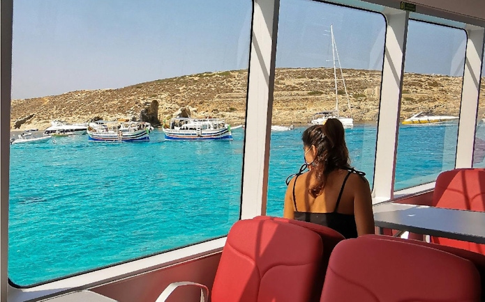 Tourist inside boat viewing Blue Lagoon's turquoise waters and rocky coastline.
