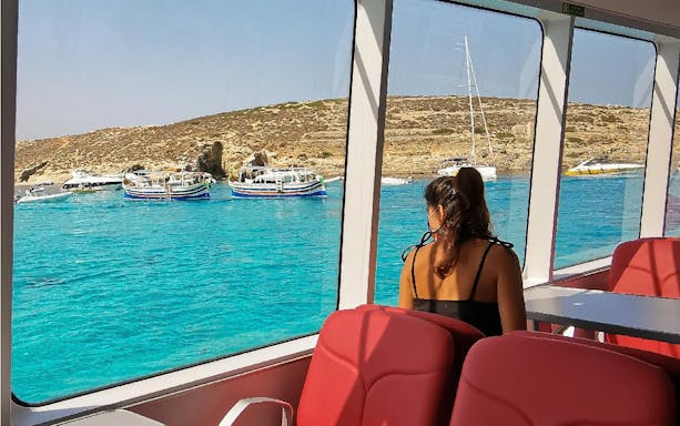 Tourist inside boat viewing Blue Lagoon's turquoise waters and rocky coastline.