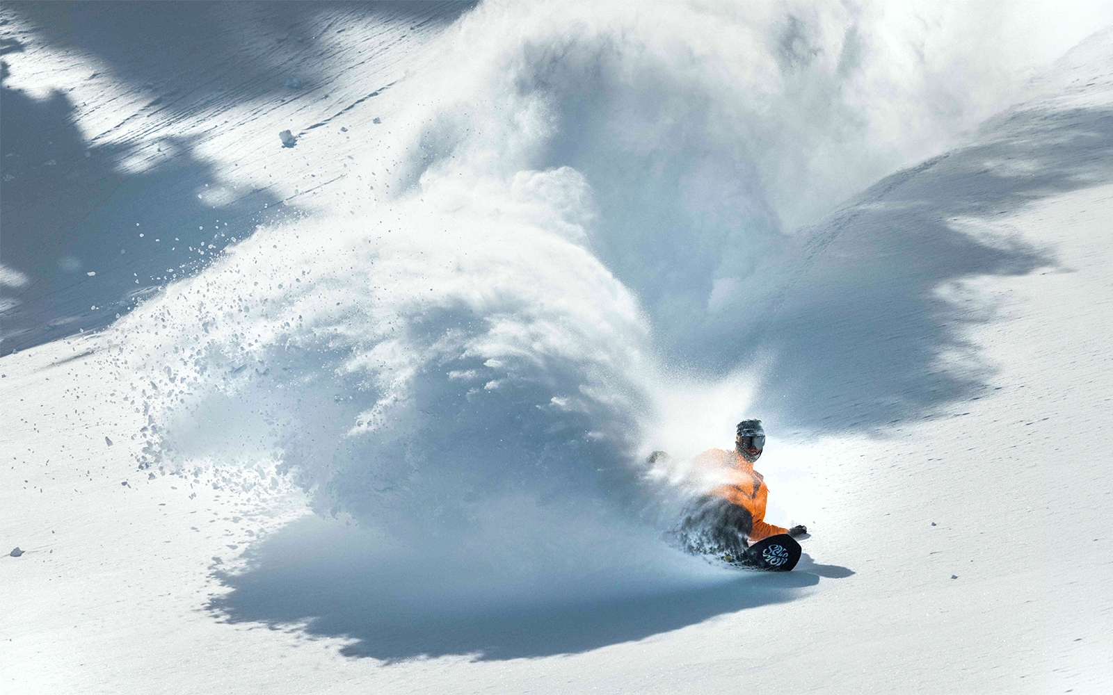 Snowboarder carving through fresh powder on a mountain slope, Ikon Pass.