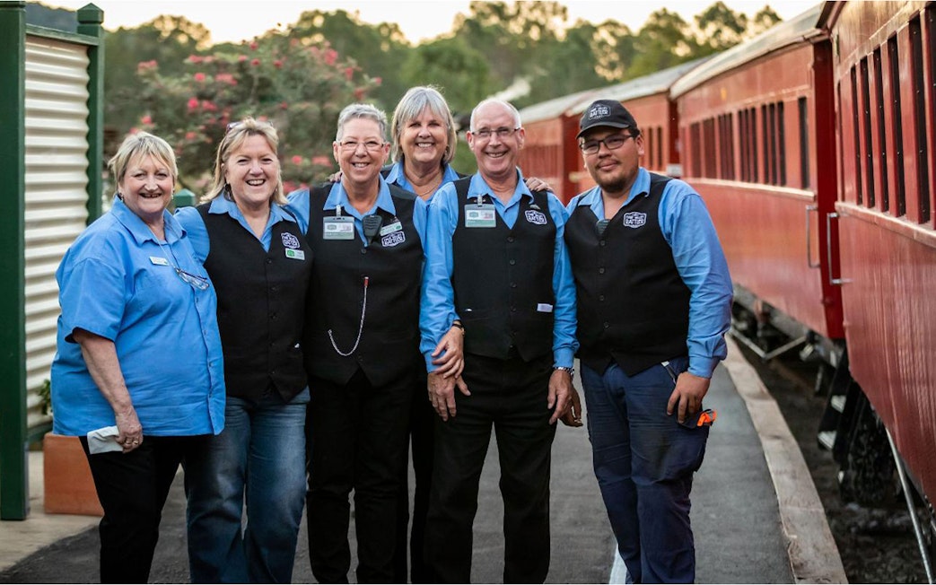 Mary Valley Rattler train crew standing beside a red train at Gympie station.