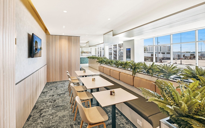 Plaza Premium Lounge seating area with tables and chairs near large windows at international arrivals.
