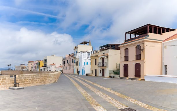 Street view of colorful buildings along the Alghero waterfront promenade.