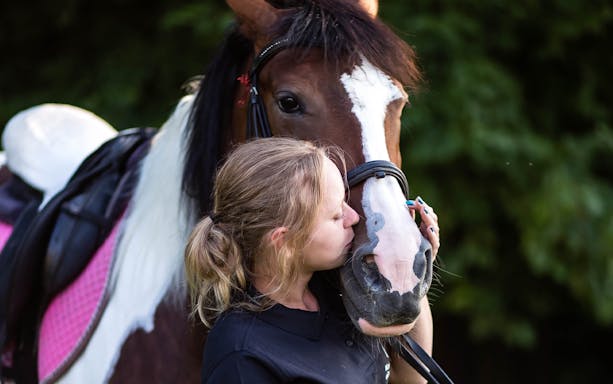 Person kissing a horse during a half-day horse riding tour near a lake in Krakow.