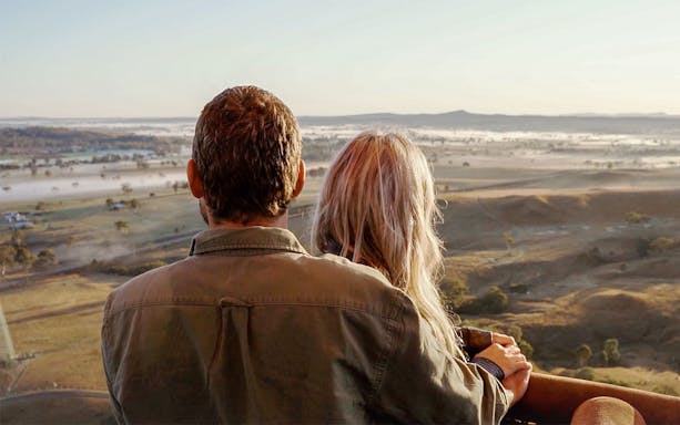 Couple enjoying a hot air balloon ride over scenic landscape.