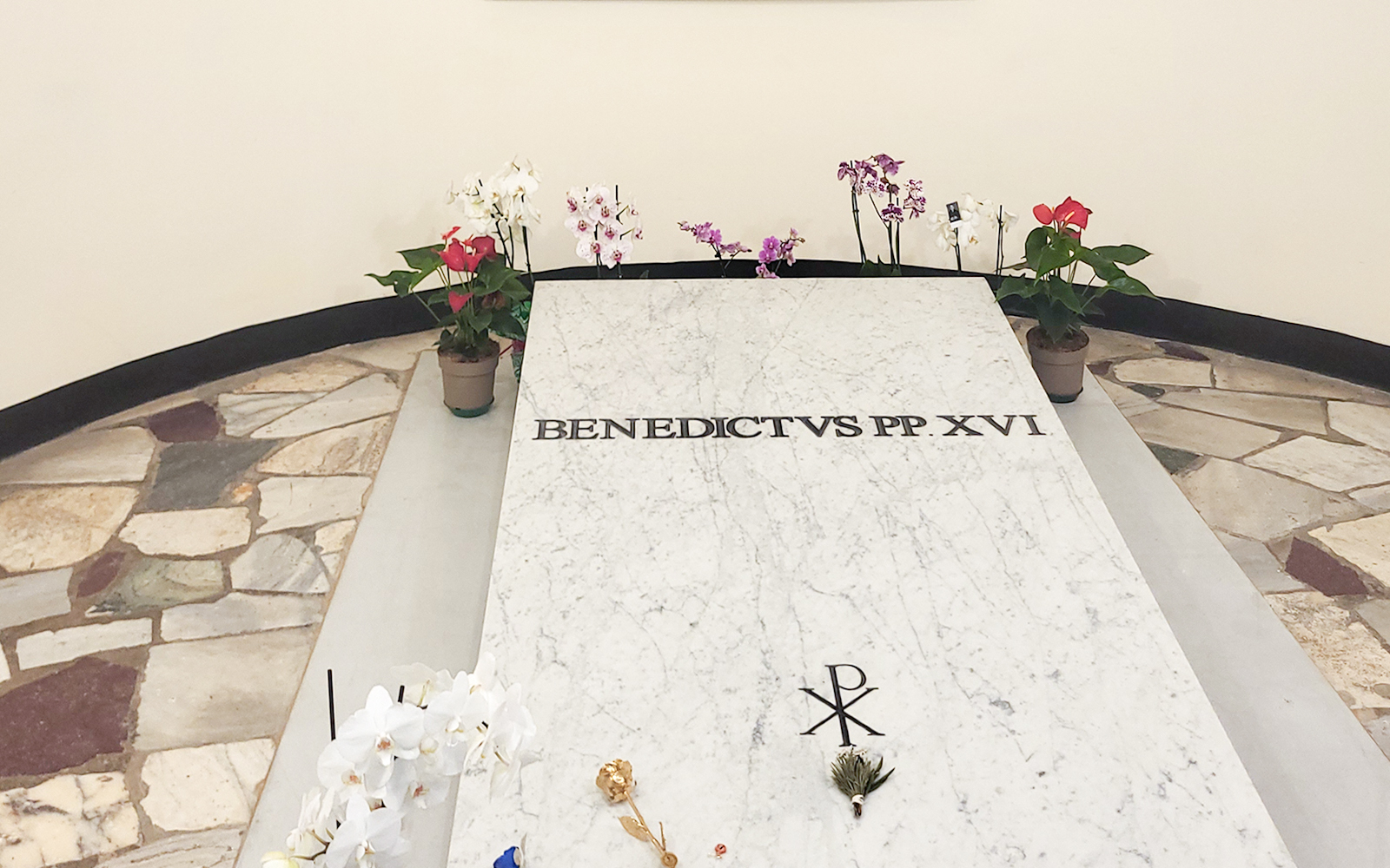 Tomb of Pope Benedict XVI in Vatican Grottoes, St. Peter's Basilica, surrounded by flowers.