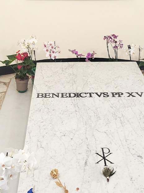 Tomb of Pope Benedict XVI in Vatican Grottoes, St. Peter's Basilica, surrounded by flowers.