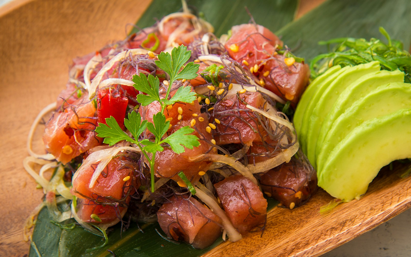 Hawaiian ahi poke with seaweed and avocado slices on a wooden plate.