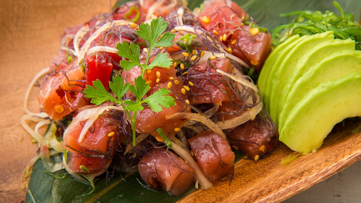 Hawaiian ahi poke with seaweed and avocado slices on a wooden plate.