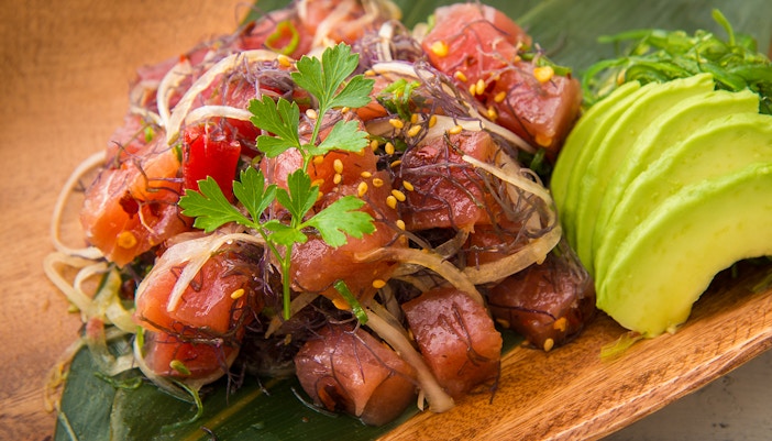 Hawaiian ahi poke with seaweed and avocado slices on a wooden plate.