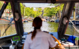 View from Amsterdam canal boat with captain steering through scenic waterways.