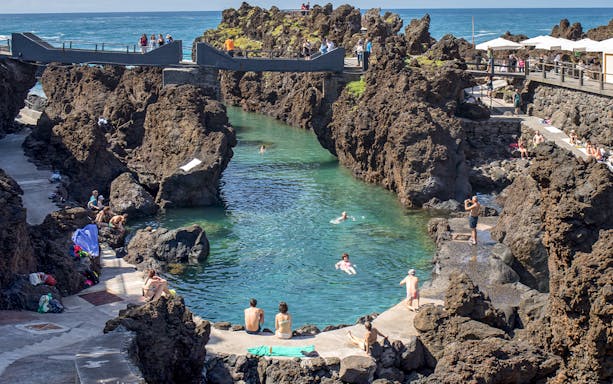 Visitors enjoying the natural lava pools at Porto Moniz, Madeira, with rocky formations and clear water.