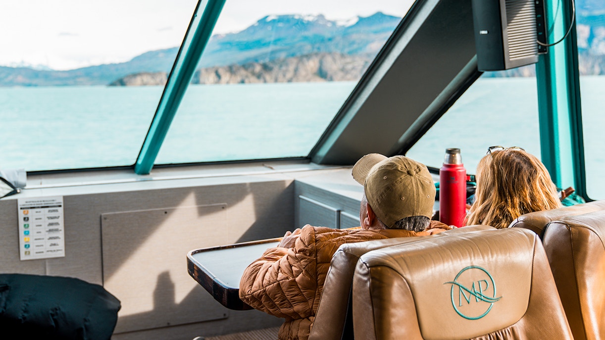Interior view of boat with passengers looking at Perito Moreno Glacier through large windows.