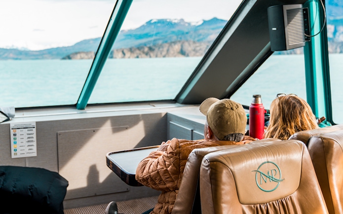 Interior view of boat with passengers looking at Perito Moreno Glacier through large windows.
