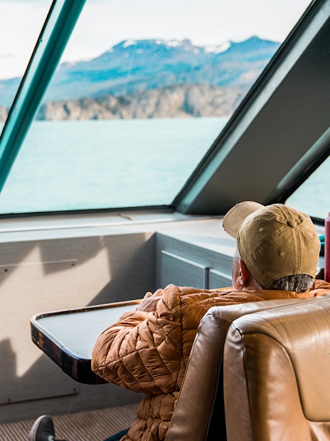 Interior view of boat with passengers looking at Perito Moreno Glacier through large windows.