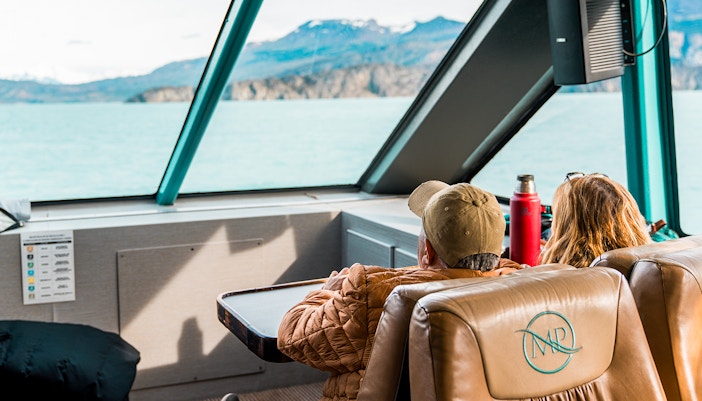Interior view of boat with passengers looking at Perito Moreno Glacier through large windows.
