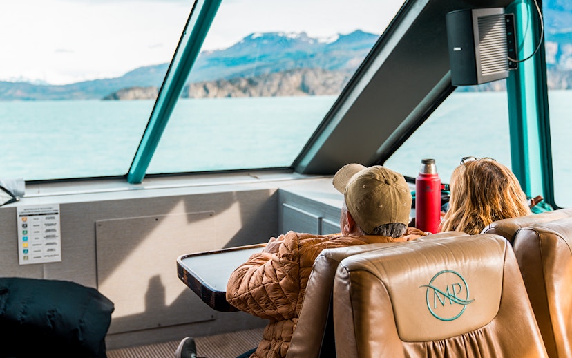 Interior view of boat with passengers looking at Perito Moreno Glacier through large windows.