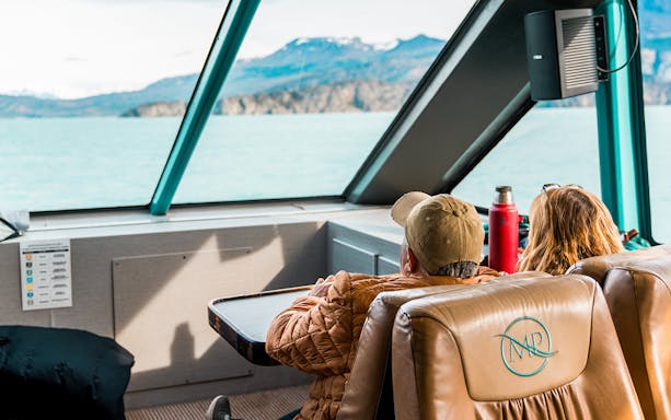 Interior view of boat with passengers looking at Perito Moreno Glacier through large windows.