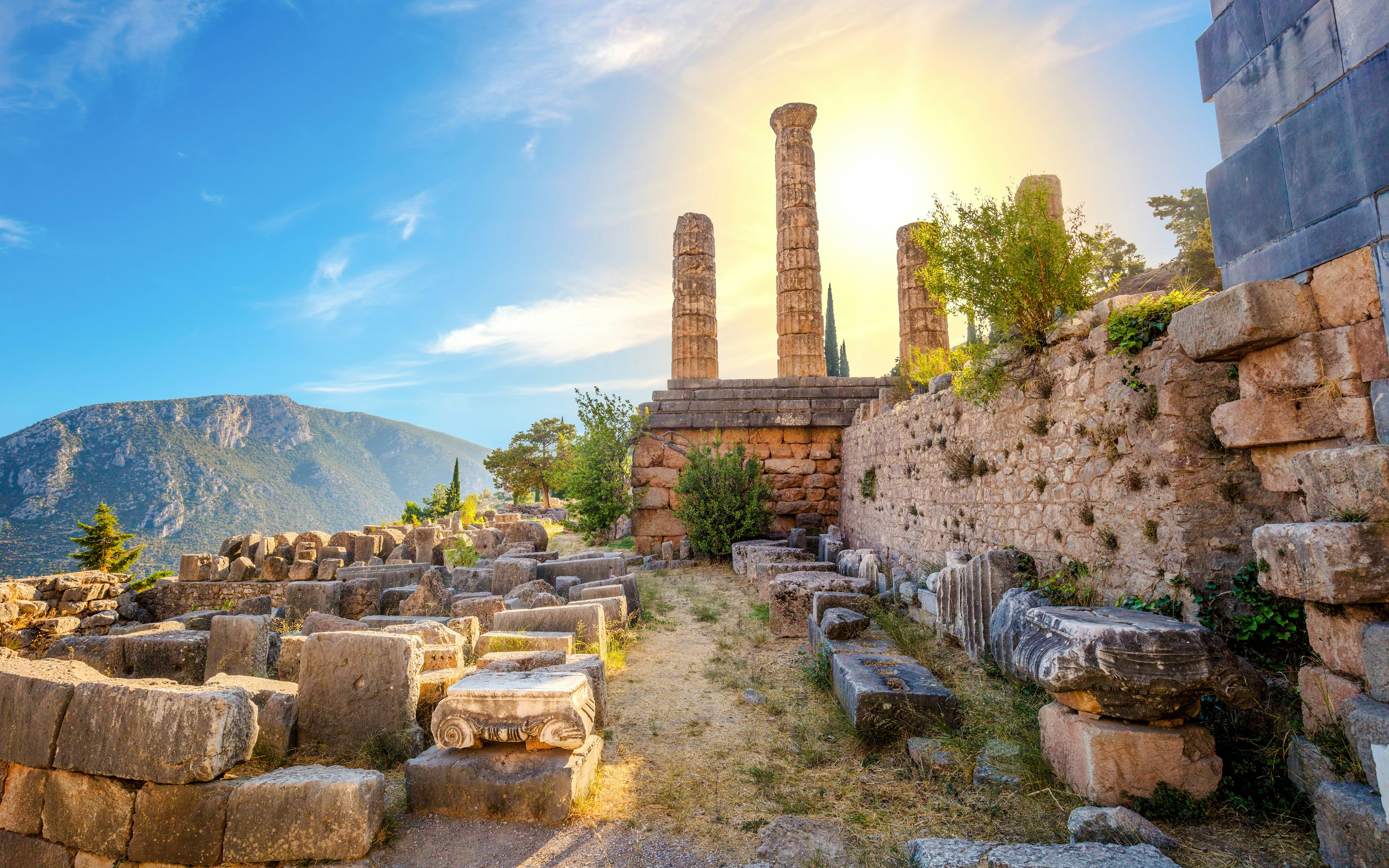 Ancient ruins of the Tholos of Athena Pronaia in Delphi with mountain backdrop.