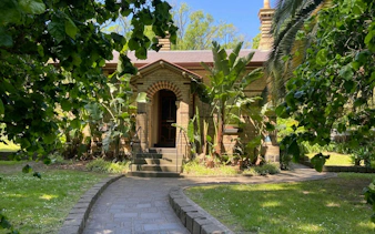 Historic building surrounded by lush greenery in Fitzroy Gardens, Melbourne.