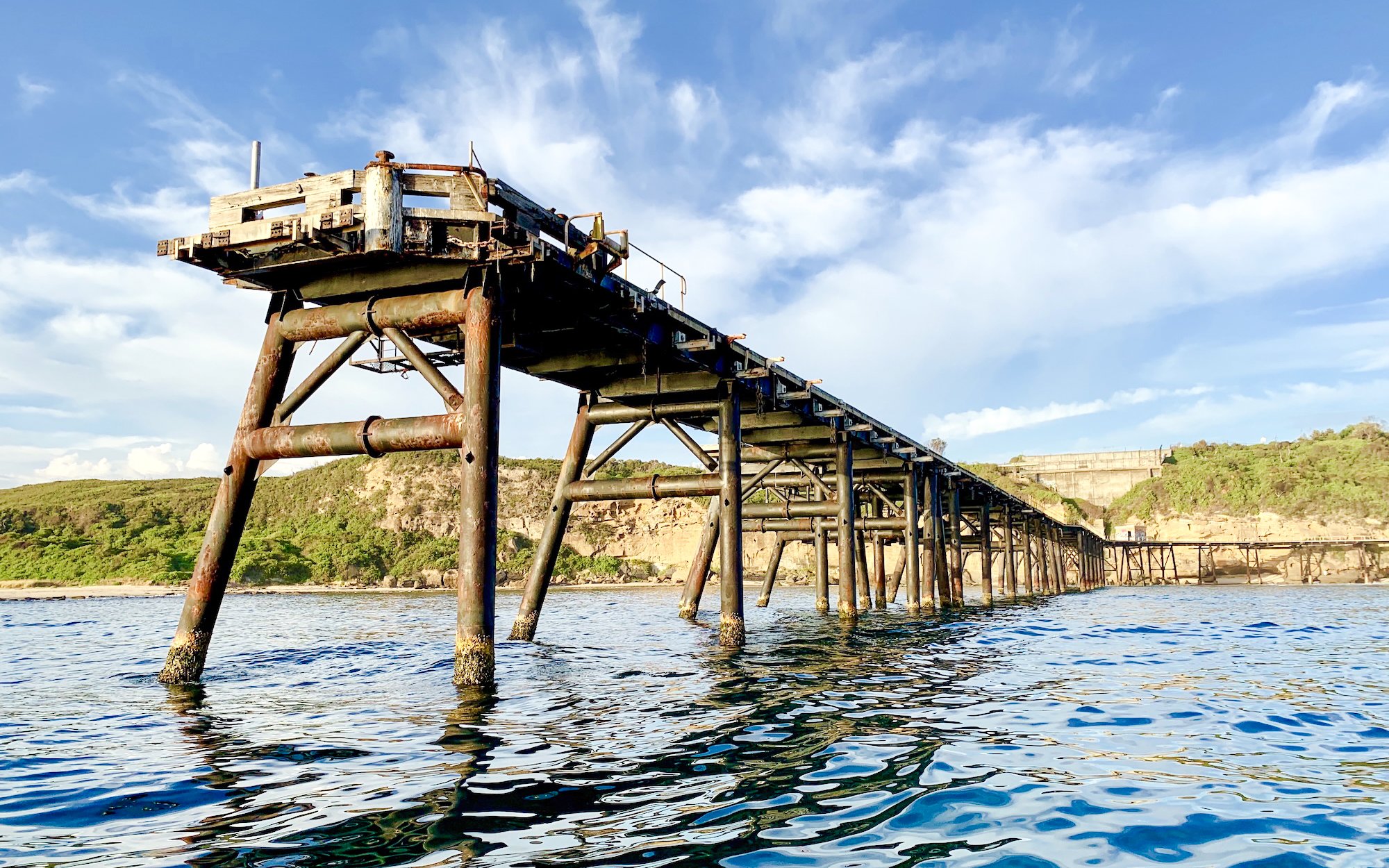 Old jetty extending into the sea near Newcastle, surrounded by cliffs and greenery.