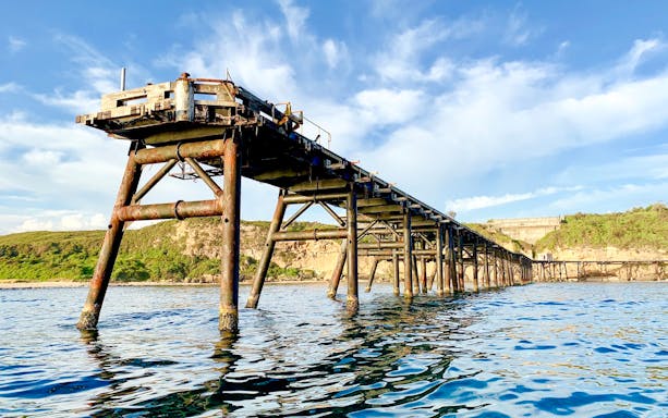Old jetty extending into the sea near Newcastle, surrounded by cliffs and greenery.