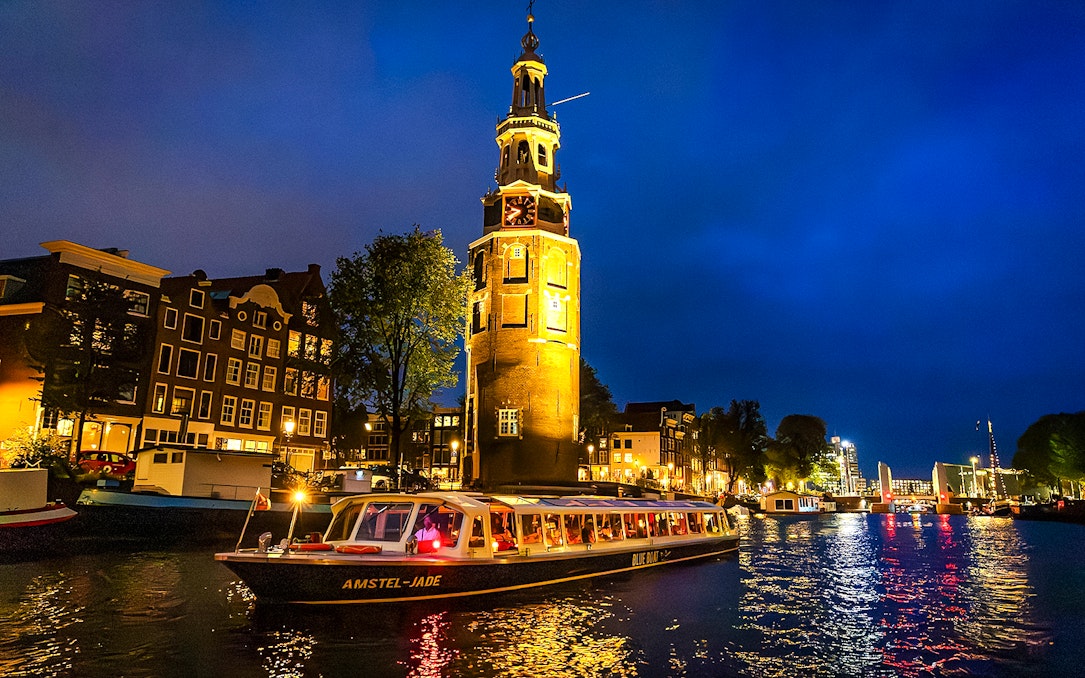 Canal cruise boat passing by Montelbaanstoren tower in Amsterdam during evening.
