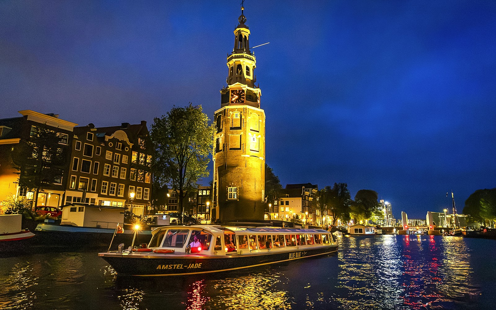 Canal cruise boat passing by Montelbaanstoren tower in Amsterdam during evening.
