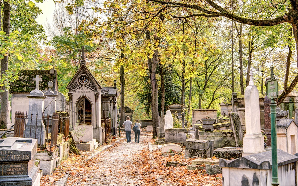 Père Lachaise Cemetery path with historic graves and autumn leaves, Paris.