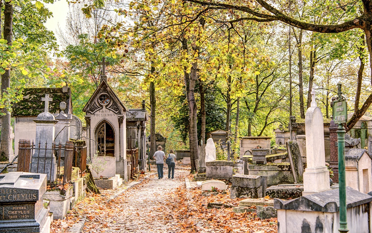 Père Lachaise Cemetery path with historic graves and autumn leaves, Paris.