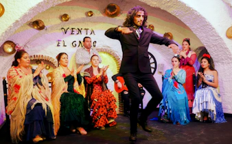 Flamenco dancer performing at Venta el Gallo with musicians and audience clapping.