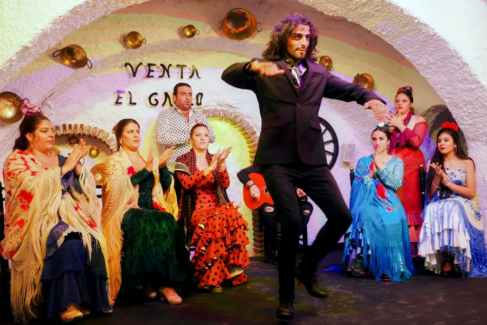 Flamenco dancer performing at Venta el Gallo with musicians and audience clapping.