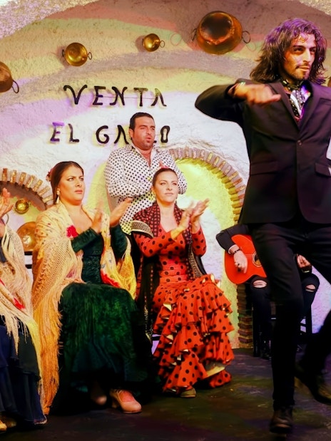 Flamenco dancer performing at Venta el Gallo with musicians and audience clapping.