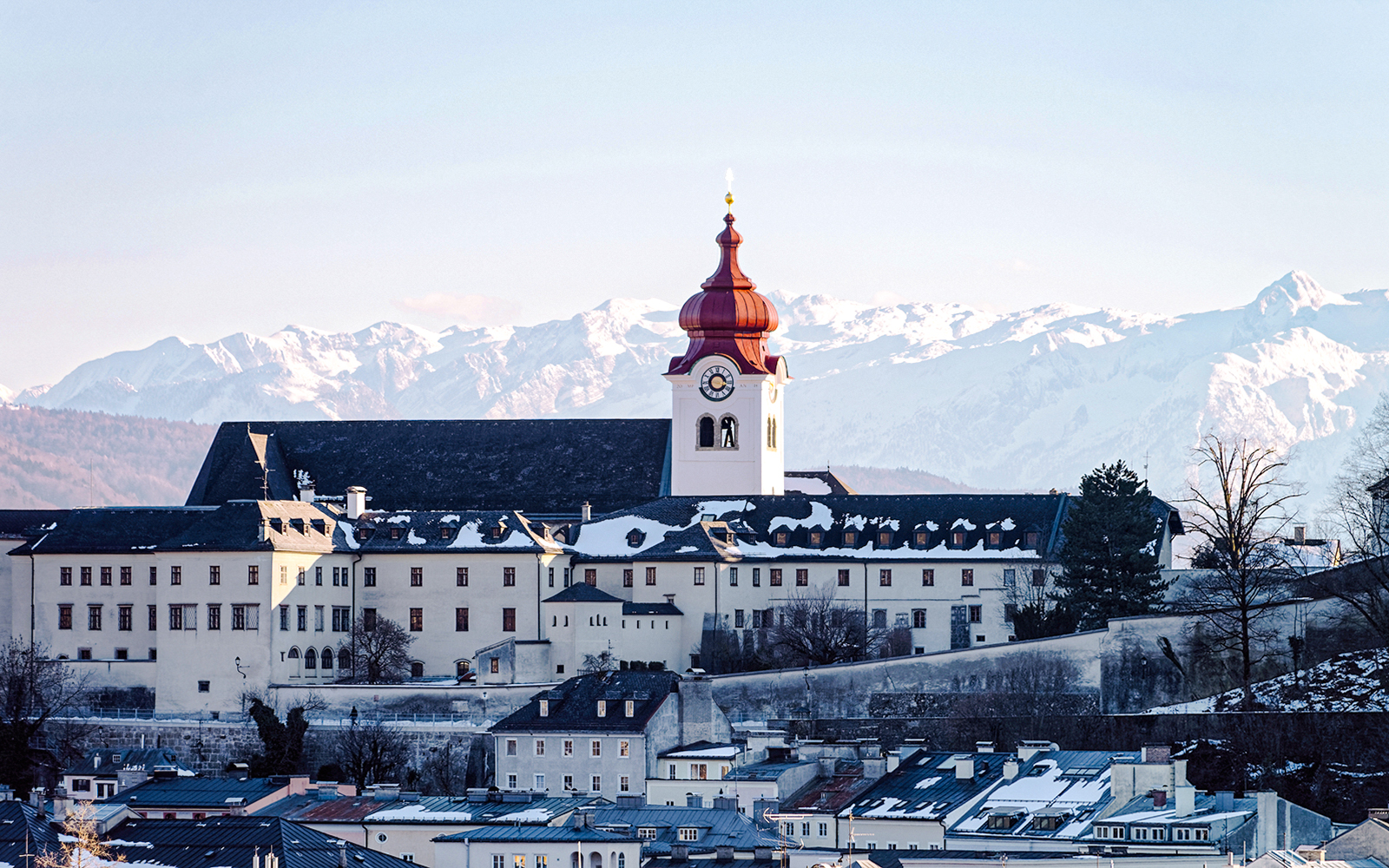 Cathedral with red dome in snowy Salzburg, Austria, with Alps in the background.
