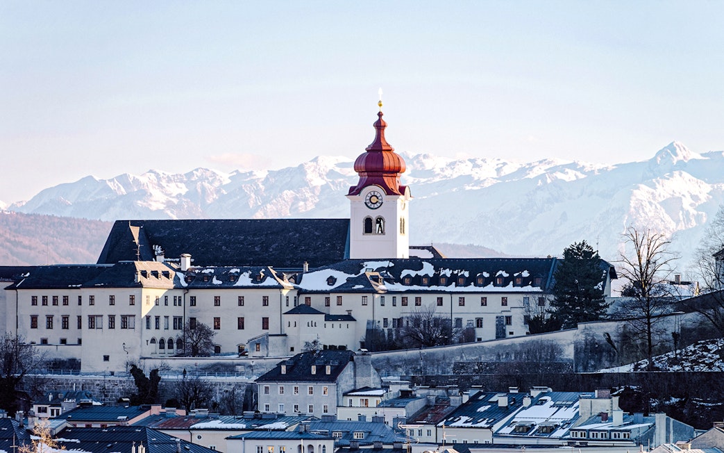 Cathedral with red dome in snowy Salzburg, Austria, with Alps in the background.