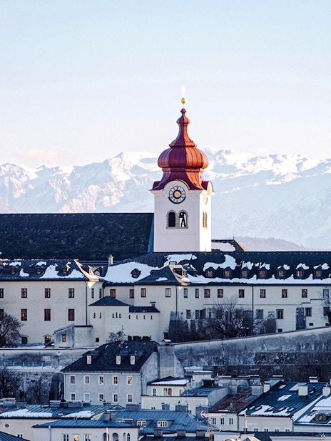 Cathedral with red dome in snowy Salzburg, Austria, with Alps in the background.
