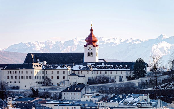 Cathedral with red dome in snowy Salzburg, Austria, with Alps in the background.
