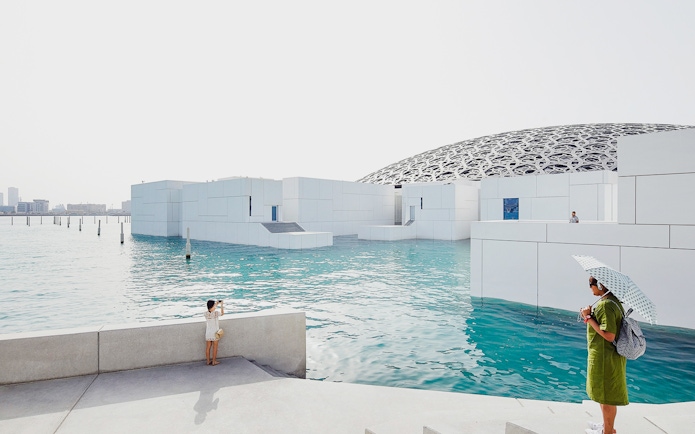 Louvre Museum Abu Dhabi with dome and water, visitors exploring the exterior.