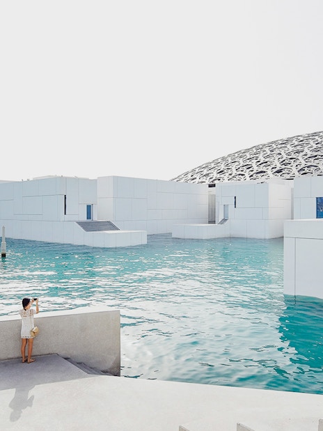 Louvre Museum Abu Dhabi with dome and water, visitors exploring the exterior.