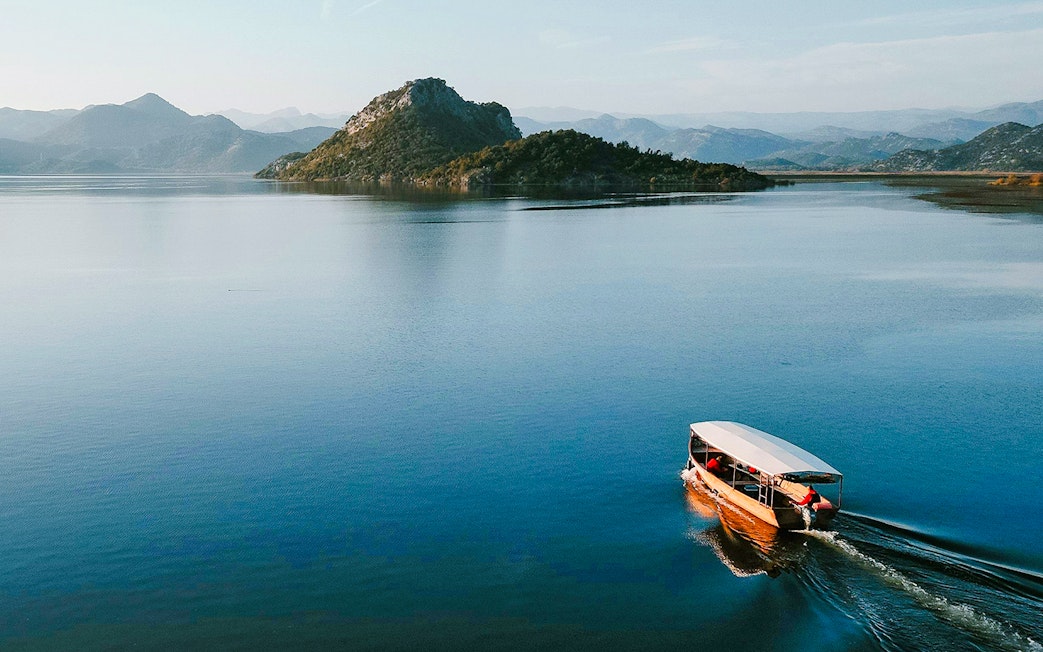 Wooden boat cruising on Lake Skadar with mountainous backdrop.