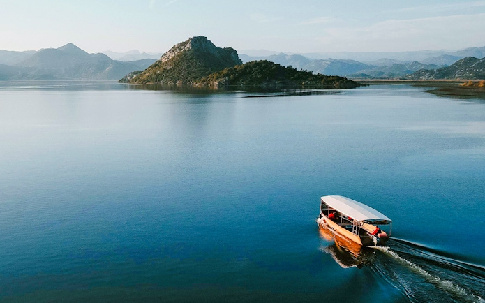 Wooden boat cruising on Lake Skadar with mountainous backdrop.