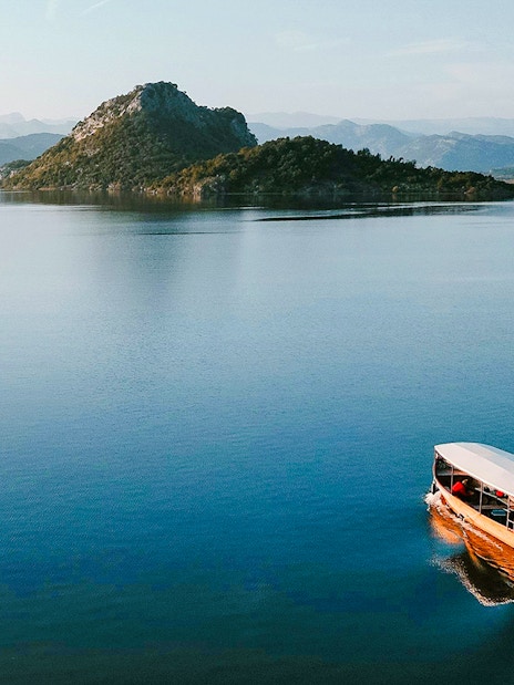 Wooden boat cruising on Lake Skadar with mountainous backdrop.