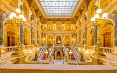 Grand Staircase in Prague National Museum with ornate decorations and golden lighting.