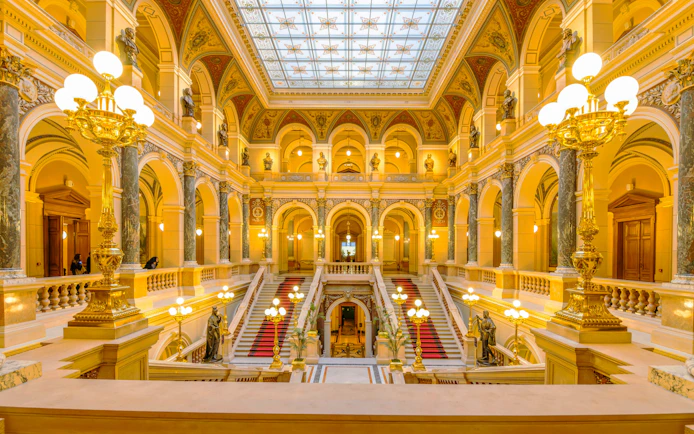 Grand Staircase in Prague National Museum with ornate decorations and golden lighting.