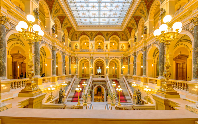 Grand Staircase in Prague National Museum with ornate decorations and golden lighting.