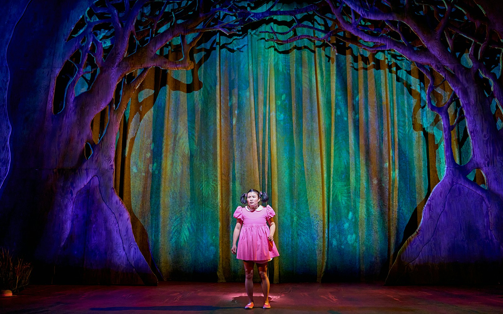 Stage scene from "My Neighbour Totoro" with character in pink dress under tree backdrop.