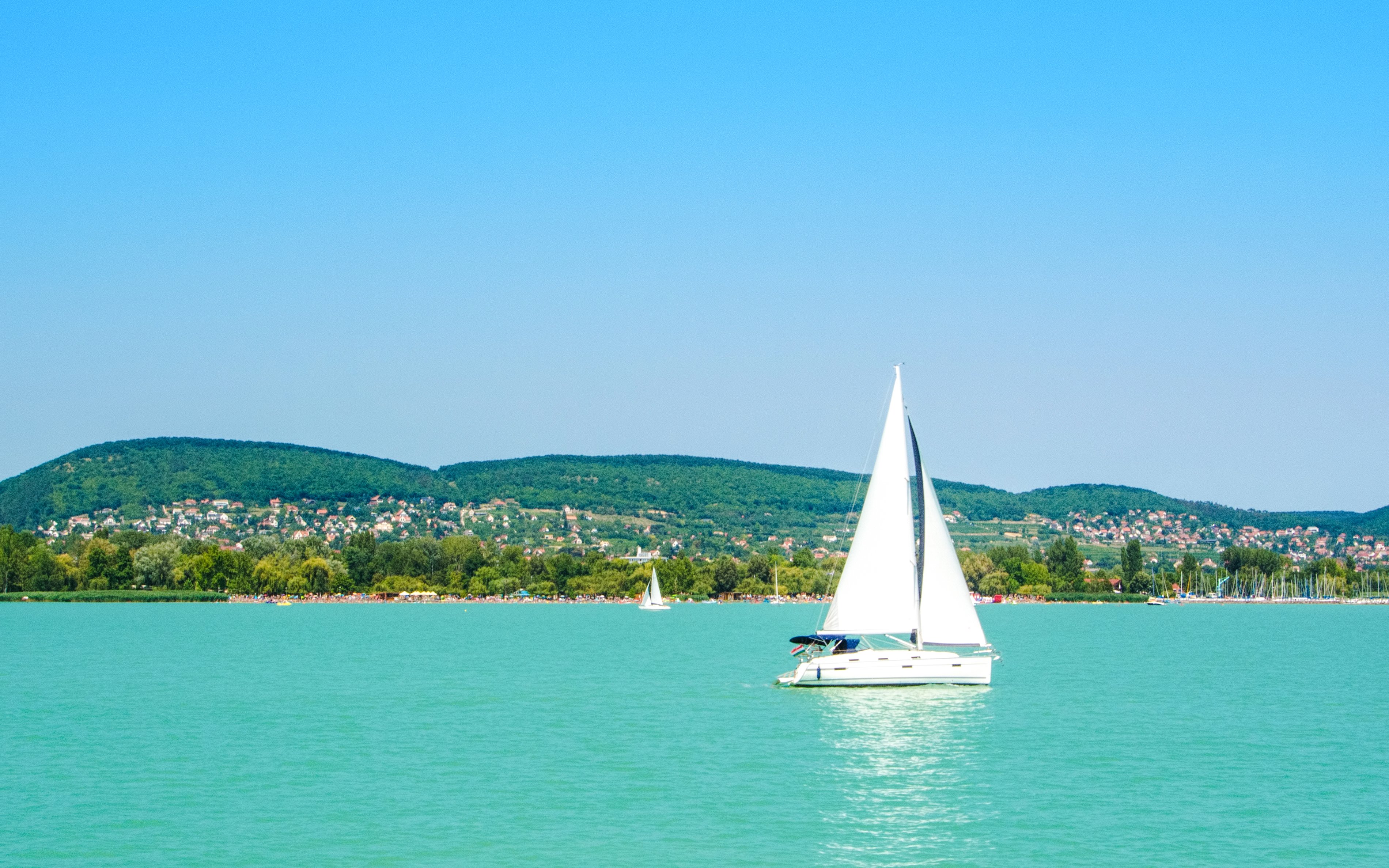 White yacht on Balaton Lake with town and hills in the background.