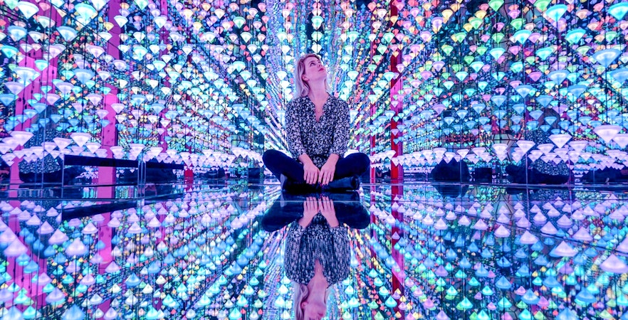 Person sitting in colorful light installation at Moco Museum Amsterdam exhibit.