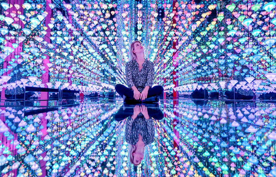 Person sitting in colorful light installation at Moco Museum Amsterdam exhibit.